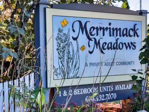 Outdoor sign for Merrimack Meadows senior living with plants nearby.