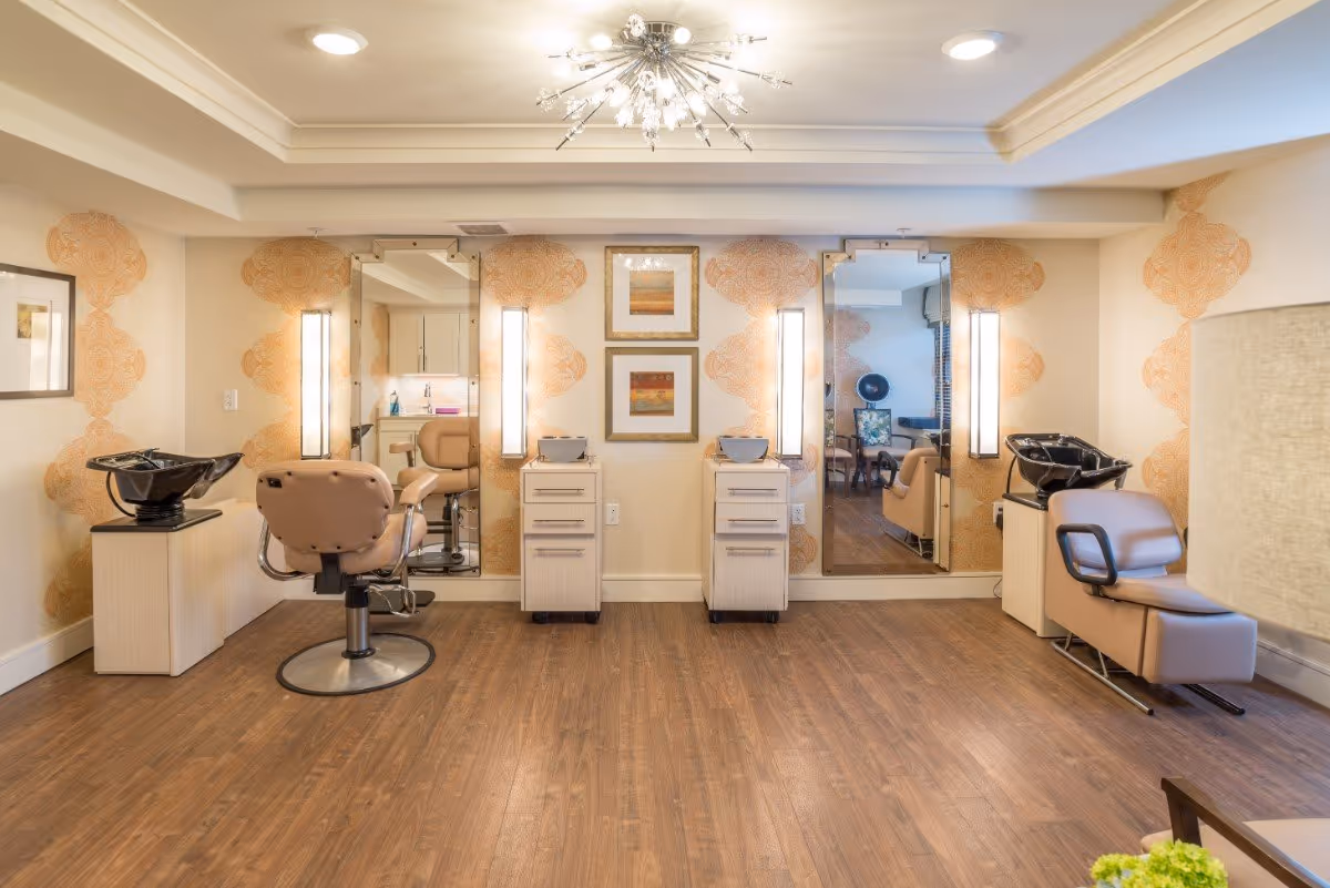 Bright salon area with two styling chairs, shampoo sinks, large mirrors and decorative wallpaper.