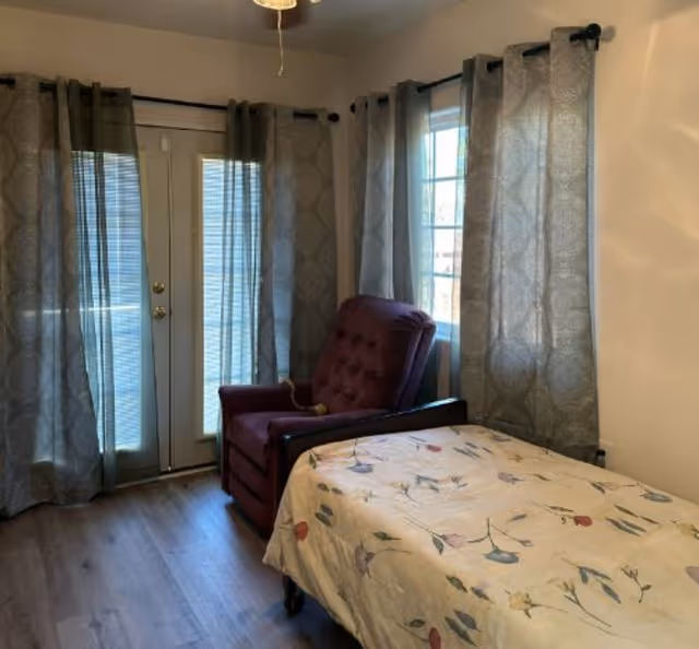 Cozy bedroom in a senior facility with a purple chair, bed, and French doors.
