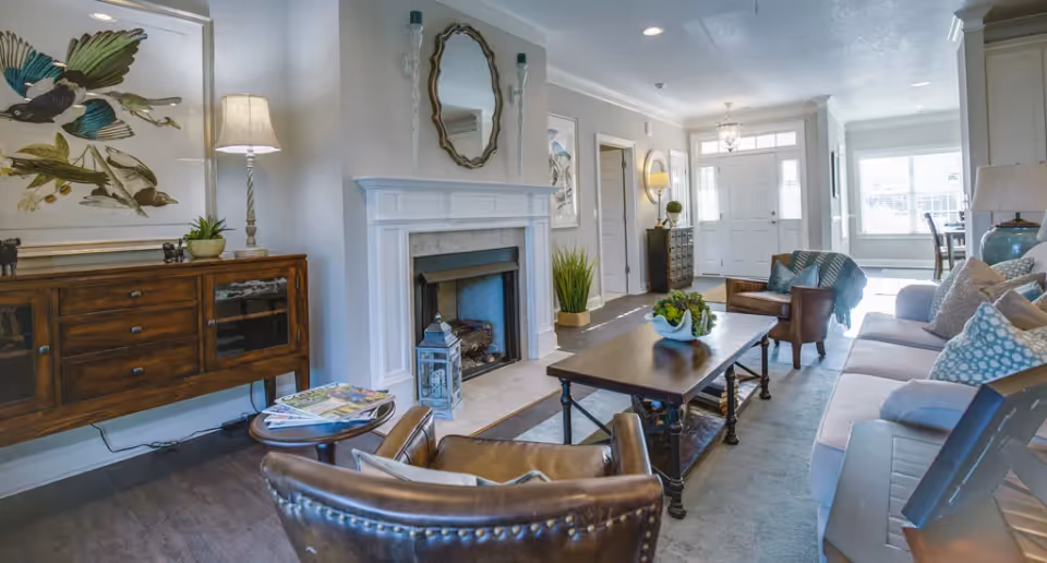 Bright furnished living room with a fireplace, sofa and chairs around a coffee table and an entry foyer visible in the background.