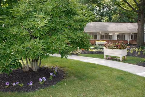 Lawn, walkway, and planters decorate the exterior of a senior living facility.