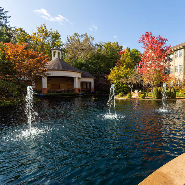 Pond with three fountains in a landscaped courtyard in front of a gazebo and an adjacent senior living building.