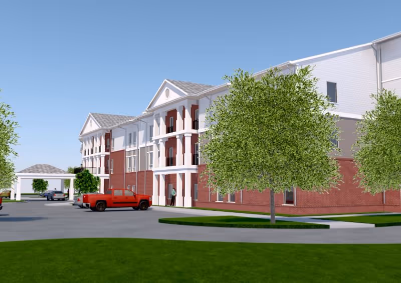 Exterior view of a brick senior living building with trees, cars, and a driveway.