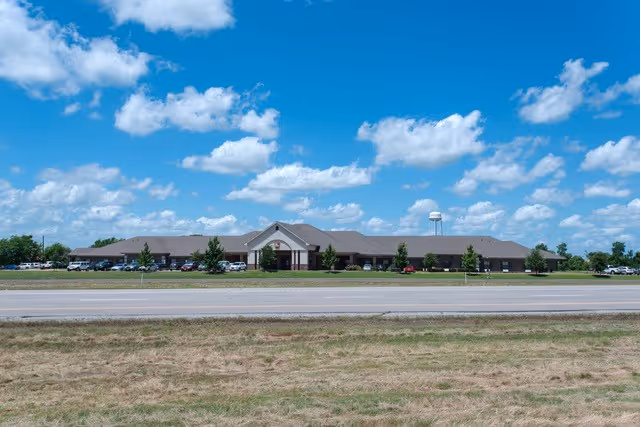 A view of the Kemp Care Center from the roadside, showing a large building under a blue sky with clouds.