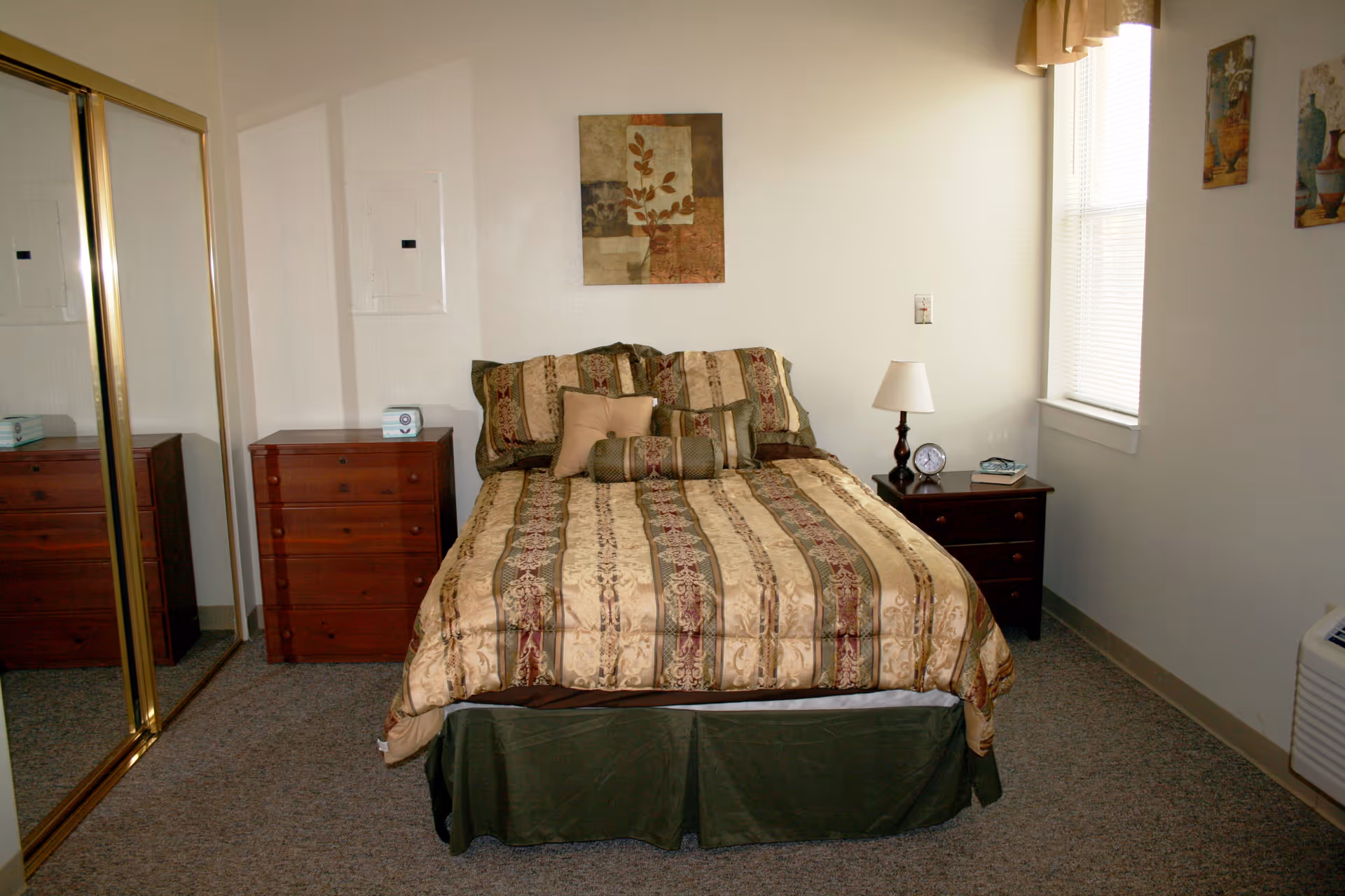 A neatly made bed with patterned bedding between two wooden nightstands in a small bedroom with mirrored closet doors.