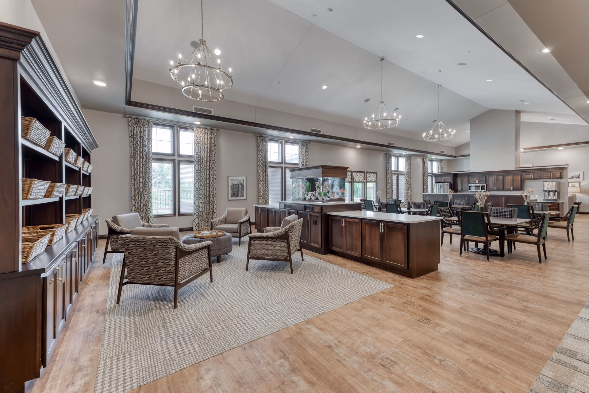 Spacious senior living common area with a seating lounge, dining tables, a central kitchen island, high ceilings and chandeliers.