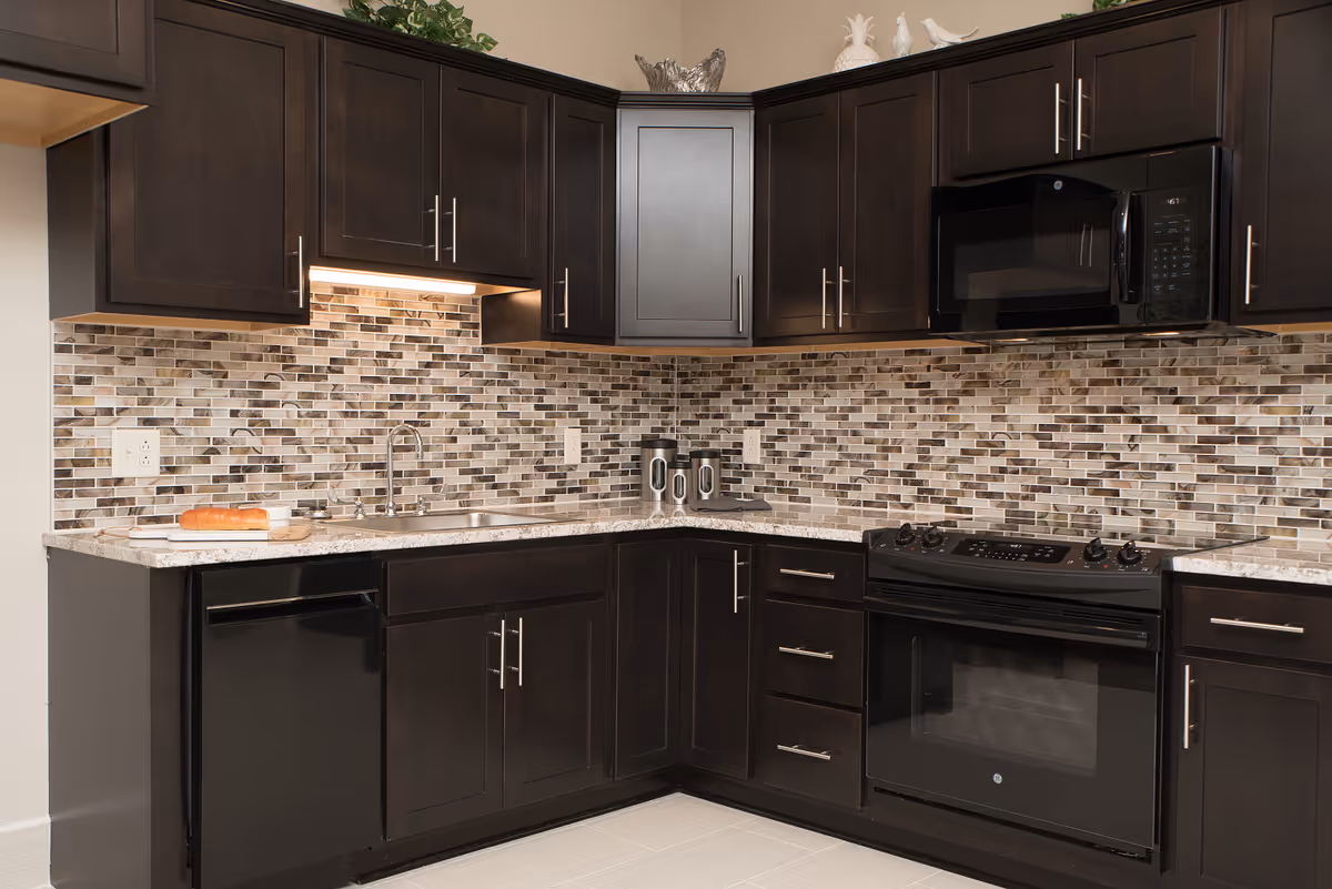 Modern kitchen with dark wood cabinets, mosaic tile backsplash, granite countertops, a sink, and black appliances.