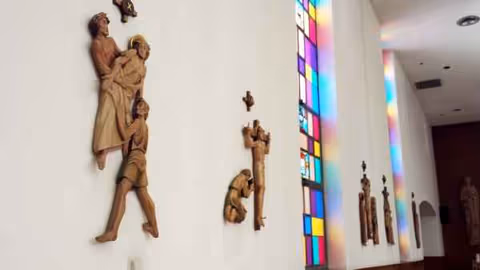 Interior hallway of Altercare Saint Joseph featuring religious statues along a white wall and stained glass.