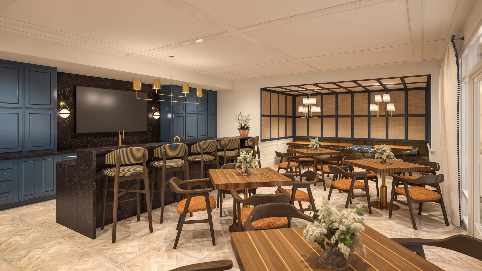 A modern dining room with wooden tables and chairs featuring orange cushions. There is a black marble counter with high chairs in front of blue cabinetry. The room has warm lighting with chandeliers and wall sconces, and a large window with a woven blind covering one wall.
