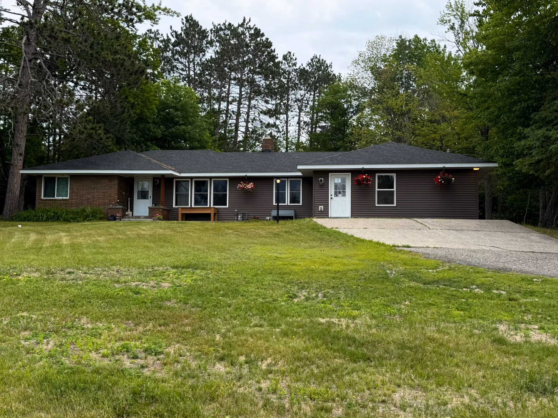 Single‑story ranch-style building with a driveway, front lawn, hanging flower baskets, and trees in the background.