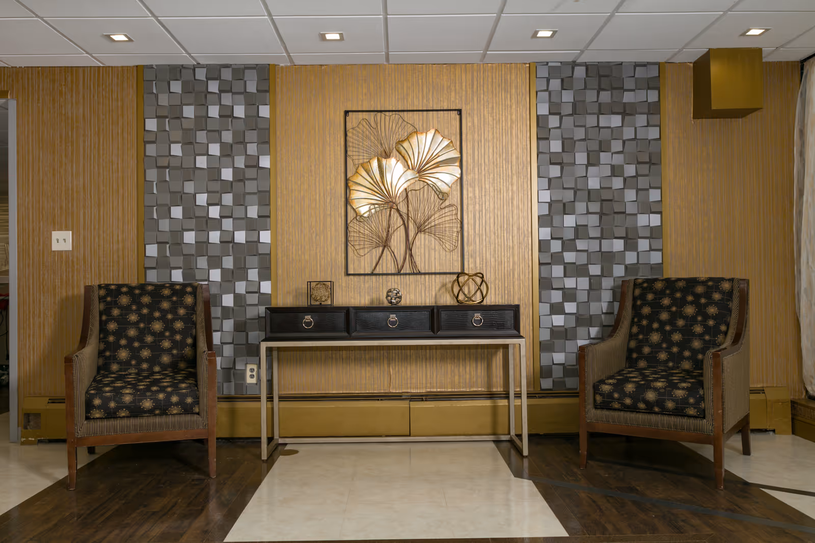 Two upholstered armchairs flank a console table with decorative objects and framed wall art in a seating area.