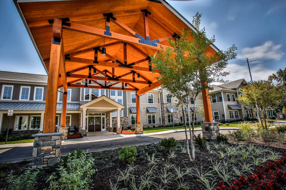 Front entrance of a senior living building with a large wooden porte-cochere and landscaped driveway.