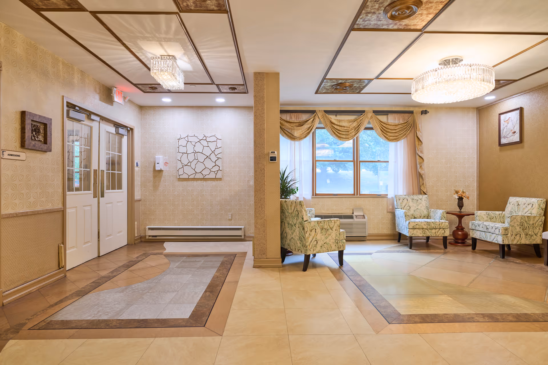 Well-lit lobby seating area with patterned armchairs, a window with drapes, and double entry doors.