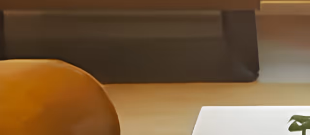 Close-up view of a wooden table with a brown leather chair on the left side and a white object with a green plant on the right side, set against a background with a dark horizontal surface.