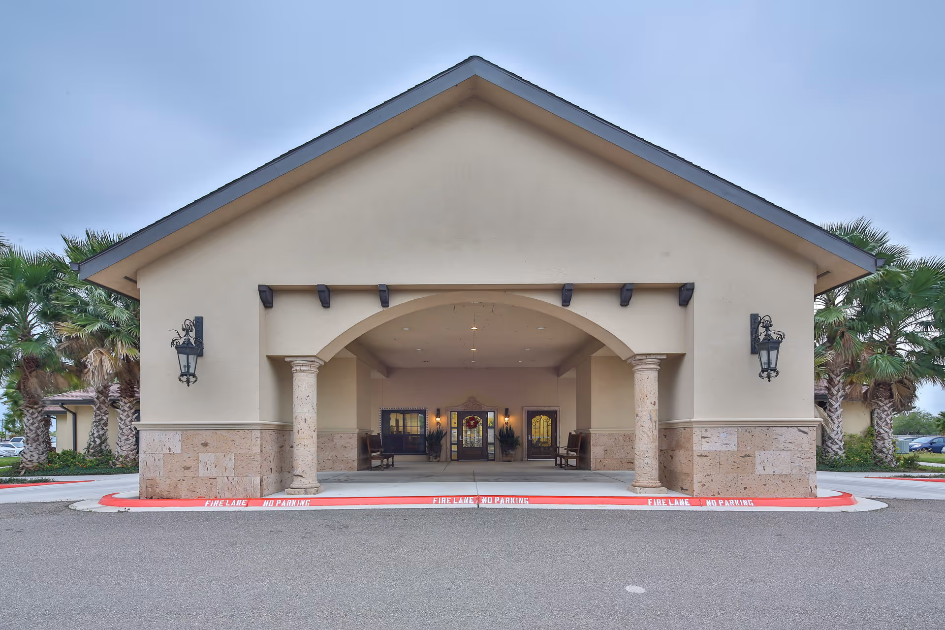 Covered entrance portico of a beige stucco building with stone columns, decorative lanterns, and a drive-through fire lane.
