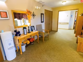 Carpeted interior hallway with a wooden console table, chairs, floral decorations and a water cooler.