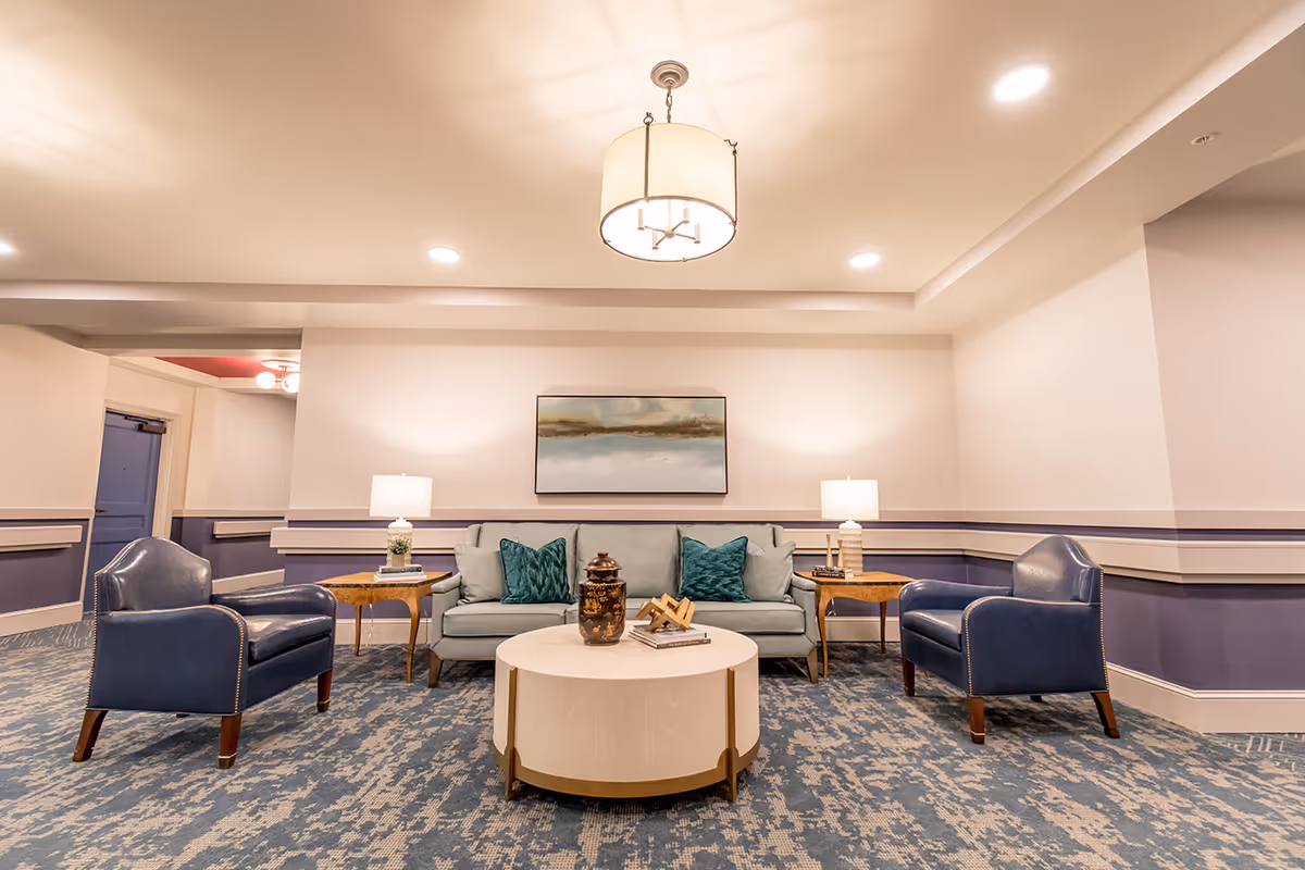 Well-lit lounge with a sofa, two armchairs, a round coffee table, side tables with lamps, and wall art.
