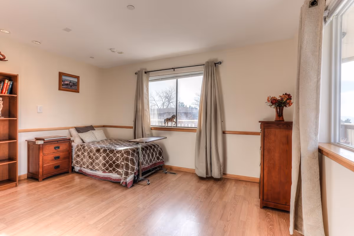 A neat bedroom with a single bed, wooden furniture, and large windows with curtains.