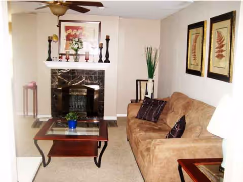 Cozy beige living room with sofa, glass coffee table, fireplace, and wall art.