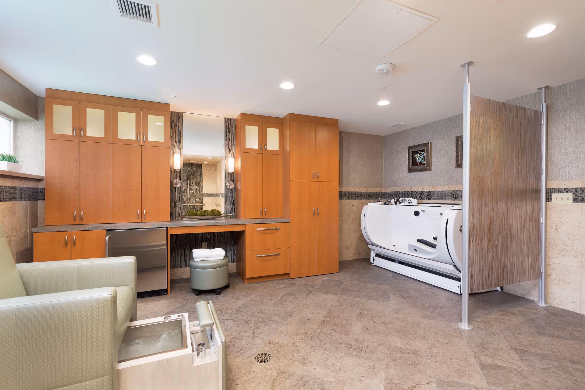 Spacious interior bathing/therapy room with wooden cabinets, a walk-in medical bathtub, seating and tiled floor.