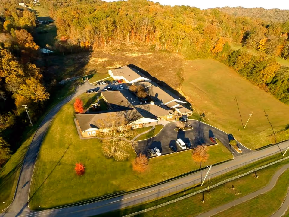 Aerial view of Jamestowne Assisted Living's single-story building with parking lot, surrounding lawns, and fall-colored trees.