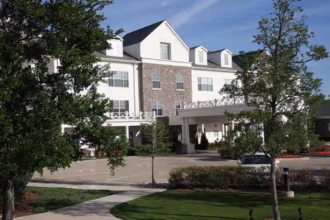 Senior living facility exterior with brick facade, covered entrance, and surrounding landscaping.