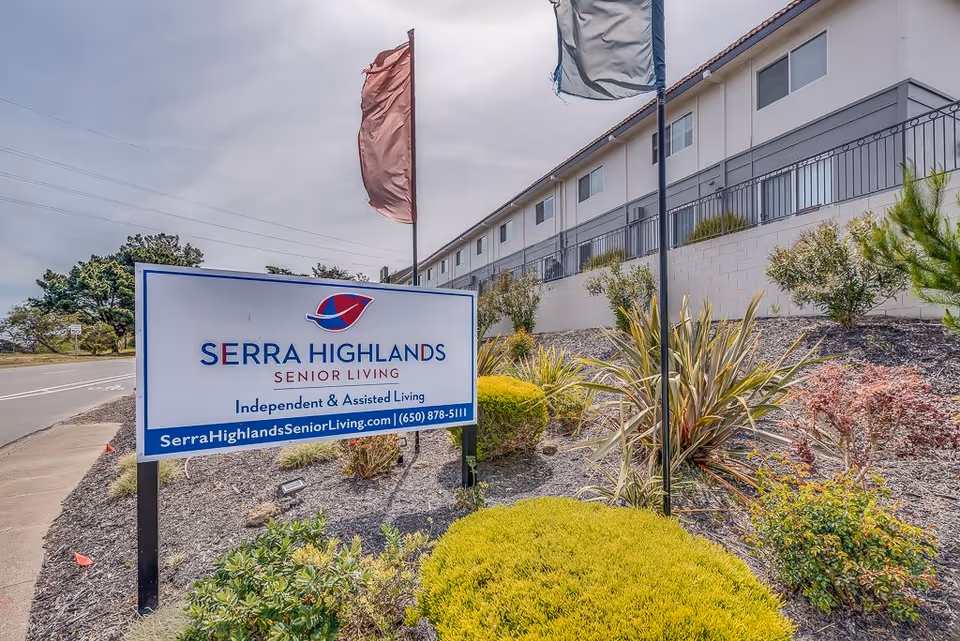 Outdoor view of Serra Highlands Senior Living facility sign with the building in the background and landscaped bushes and plants around the sign.