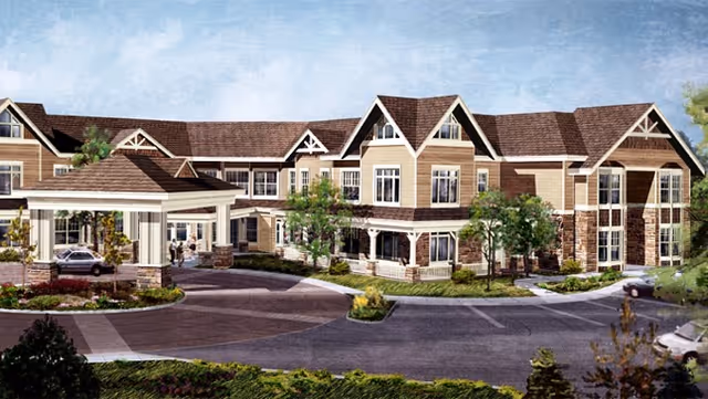Front exterior of a multi-story assisted living building with a covered porte-cochere, landscaped driveway, and gabled roofs.