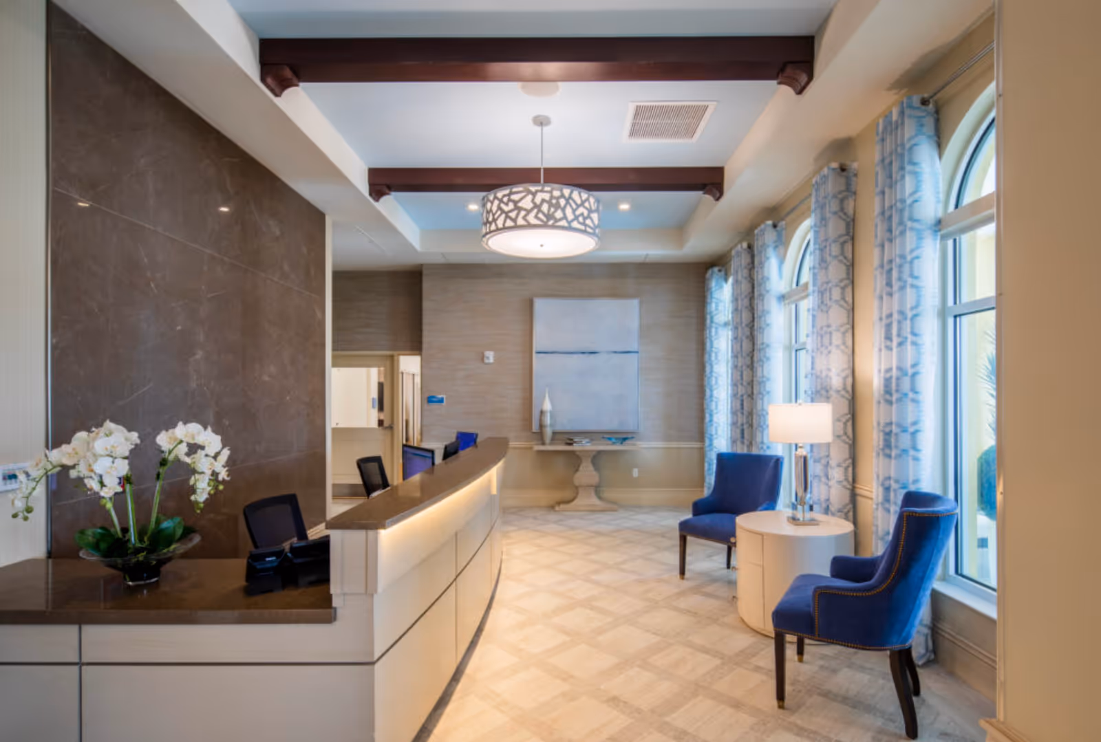 Reception lobby interior with a curved front desk, white orchids, and blue chairs by arched windows.