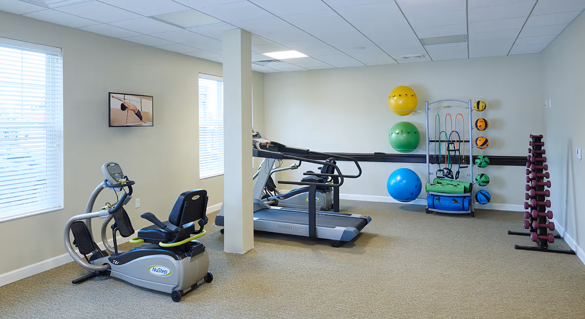 Well-lit fitness room with a treadmill, recumbent bike, a rack of dumbbells, and several exercise balls and accessories.