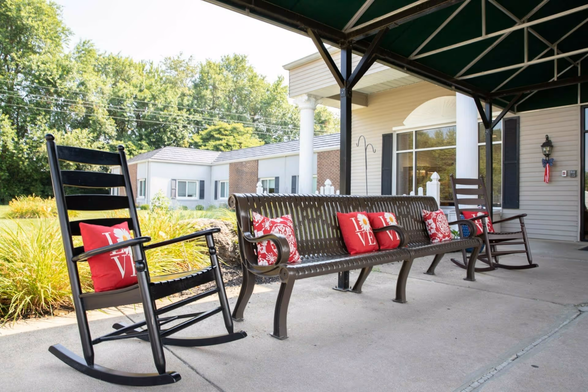 Covered front porch at the Williamsport facility with rocking chairs and a metal bench adorned with red decorative pillows.