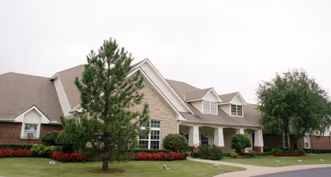 Front exterior of a single-story brick and stone senior living building with a lawn, trees, and a covered entrance.