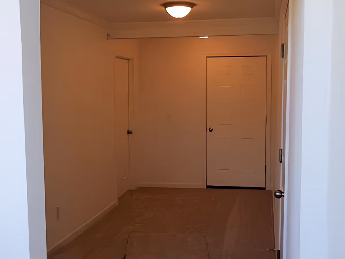 A narrow hallway with beige walls and carpeted floor, featuring three closed white doors and a ceiling light fixture.