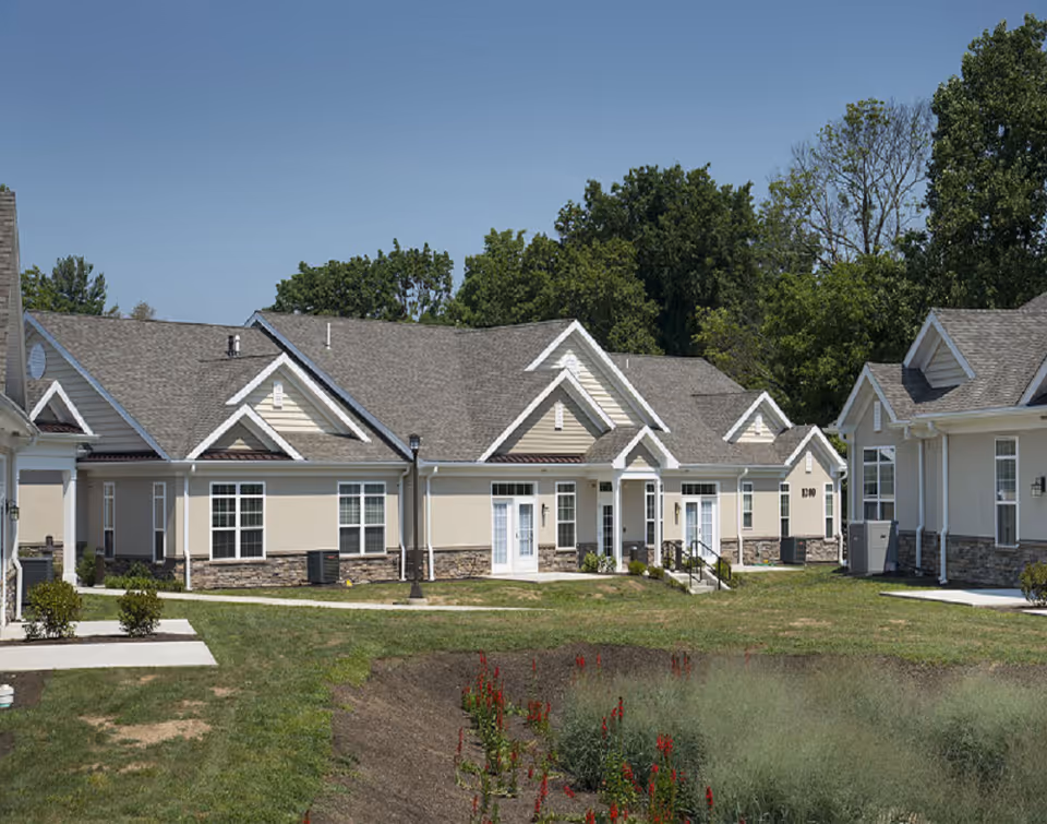 Row of beige senior living cottages with gabled roofs and green lawn.