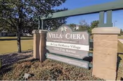Outdoor view of a sign for Villa Ciera at Lou DeMarco Village, located at 1199 27th Avenue, surrounded by grass, trees, and a clear blue sky.