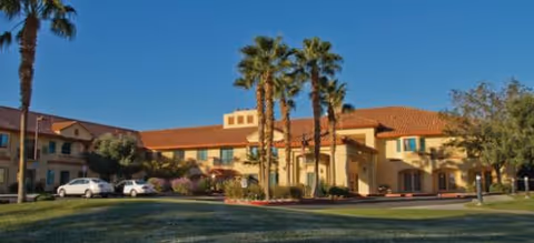Exterior view of The Havens at Antelope Valley, tan stucco senior living facility with palm trees.