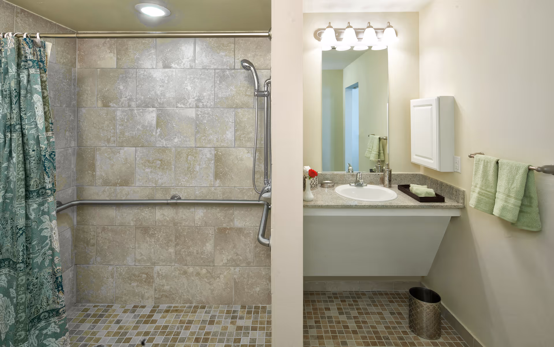 Accessible bathroom featuring a tiled walk-in shower with grab bars and a vanity with sink and mirror.