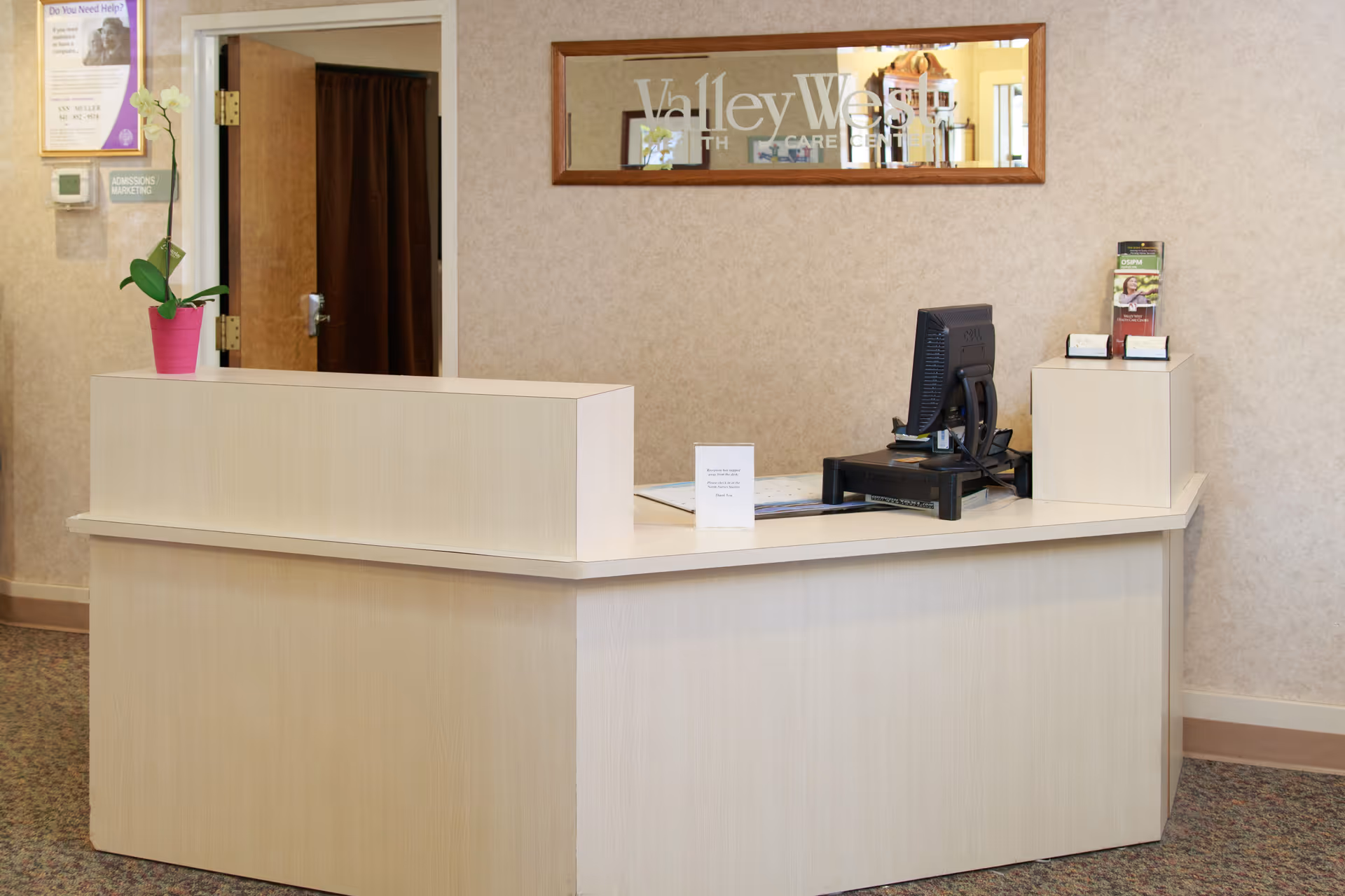 Reception desk in a healthcare facility lobby with a computer, brochures, and a mirror reading "Valley West".