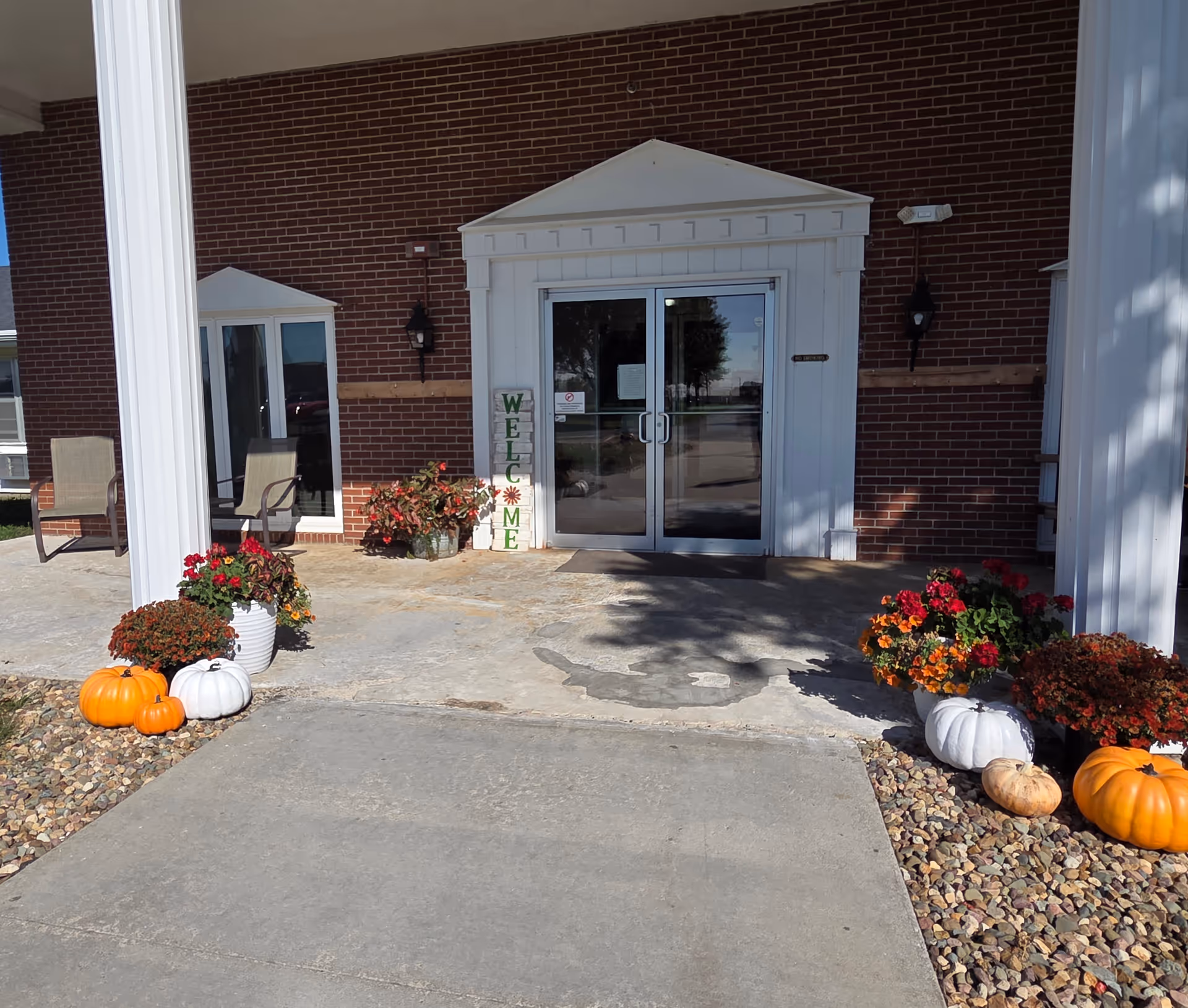 Entrance of Maple Heights Nursing & Rehabilitative Center featuring a welcome sign, potted flowers, and pumpkins.