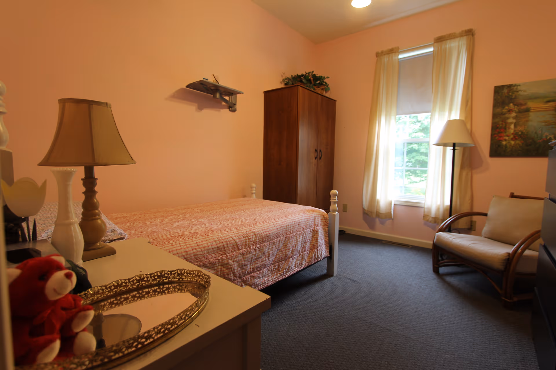 Cozy single-occupancy bedroom with a bed, wardrobe, armchair, bedside lamps, and a curtained window.