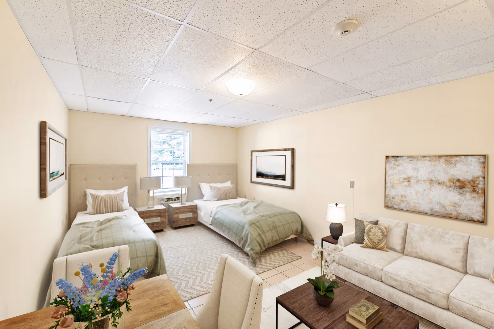 Bright furnished studio-style senior living room with two twin beds, a sofa and coffee table, and a small dining table by a window.