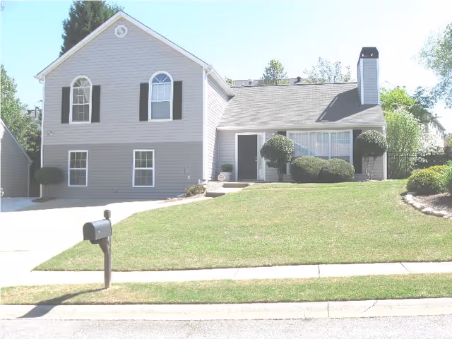 Front view of a two-story suburban house with a sloped lawn, mailbox, and trimmed shrubs.