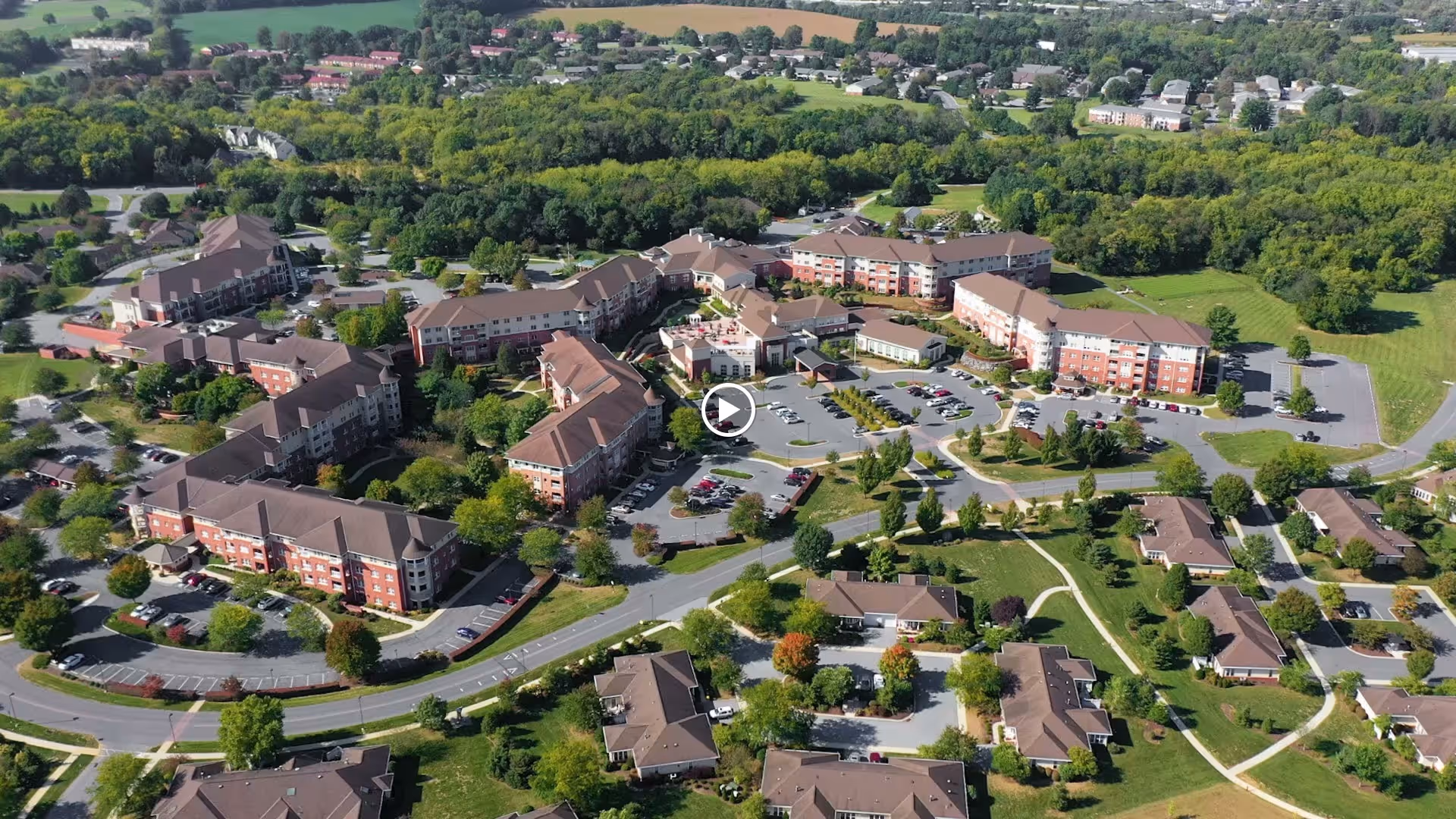 Aerial view of a large senior living campus with multiple connected brick buildings, parking lots, and landscaped grounds.