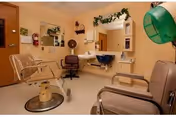 A small salon room with styling chairs, mirrors, a hair-washing sink, and a green hooded hair dryer.