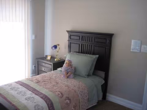 Cozy bedroom with dark wood headboard, matching nightstand, bedside lamp, and floral quilt.