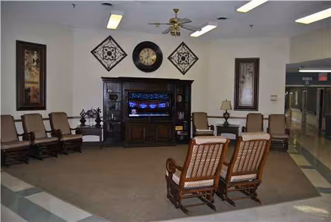 Cozy senior living lounge with chairs around a central entertainment cabinet and wall decor.