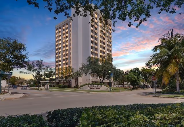 Exterior view of a tall multi-story building named Imperial Club at sunset, surrounded by trees and greenery, with a clear sky showing some clouds.