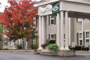Covered entrance of Summercrest Senior Living Community featuring white columns, planters, and a red-leaved tree.