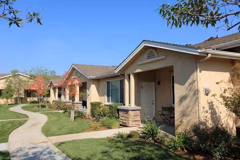 Row of beige senior apartment buildings with covered front porches and a winding sidewalk.