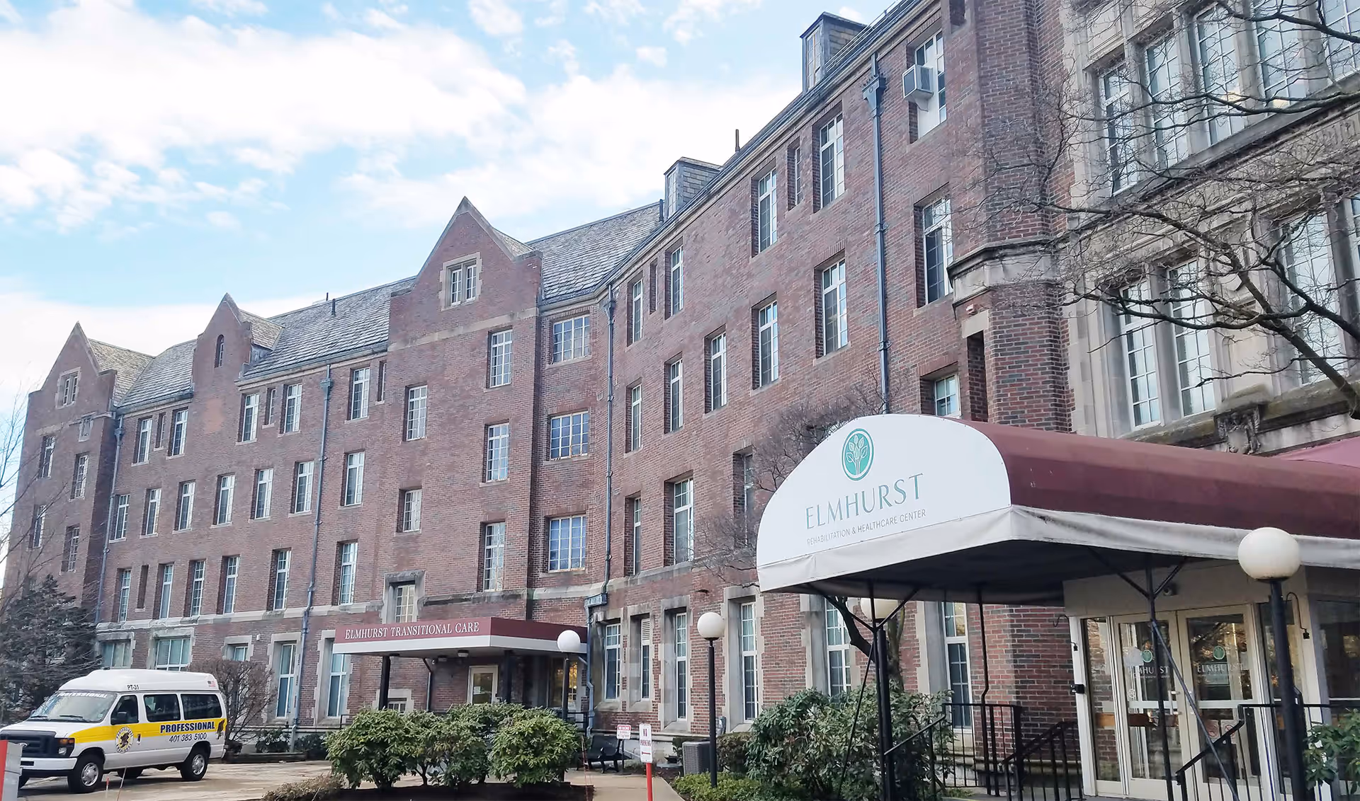 Exterior view of Elmhurst Rehabilitation & Healthcare Center, a large multi-story brick building with multiple windows and a maroon awning over the entrance. A white van is parked near the entrance, and some bushes and trees are visible in front of the building under a partly cloudy sky.